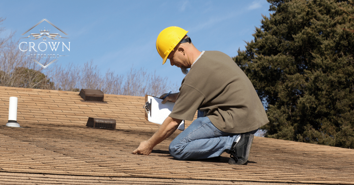 a man kneeling on the roof, inspecting the roof's quality, with a clipboard in hand