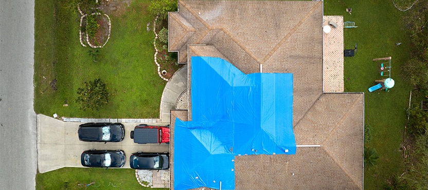 overhead view of a house with blue tarping on a roof, to show ongoing repair