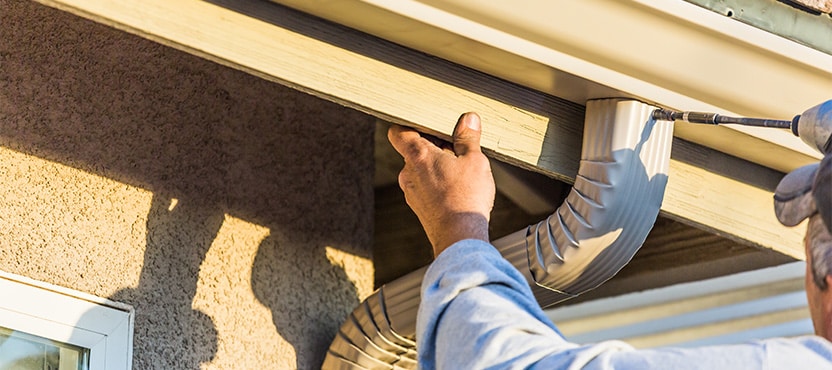 a contractor screws in a gutter to the side of a house