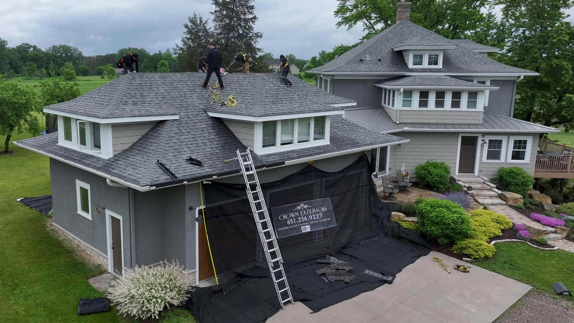 crown exteriors contractors installing a new roof on a restidential house iwth beautiful gardens, and a porch